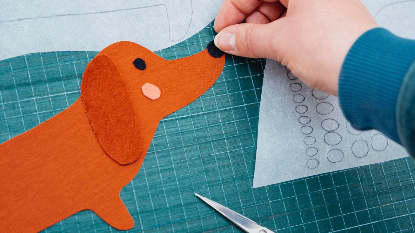 Faire Kleidung in Deutschland produziert von internaht in Dresden - von Hand ausgeschnittener Dackel aus verschiedenen Biostoffen, bei dem von Hand die letzten Applikationsteile gelegt werden.