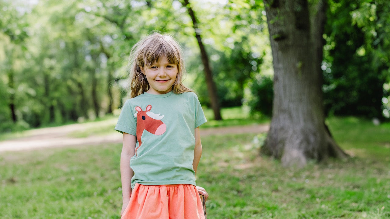 Nachhaltige Kindermode von internaht aus Dresden - Mädchen trägt hellgrünes Kinder T-Shirt mit liebevollen Pferde-Motiv und orangefarbenen Stufenrock aus Bio Baumwolle. Alles von internaht