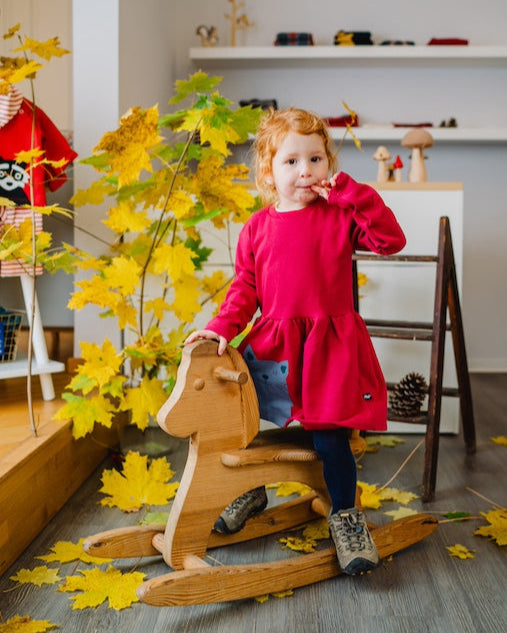 Größentabelle Babys für Bio Babykleidung von internaht - kleines Mädchen im Kleid mit Katze auf Schaukelpferd im internaht Atelier