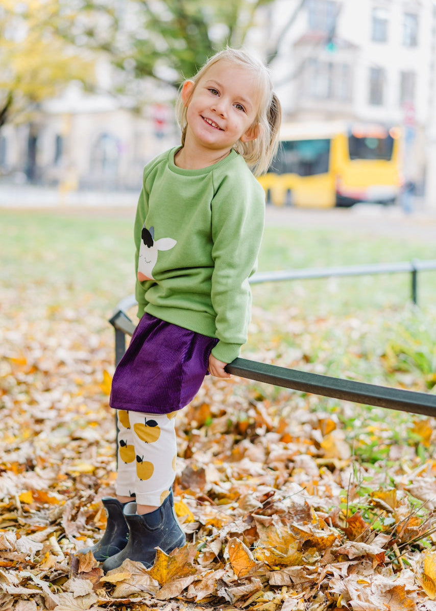 Kinderoutfit mit grünen Sweater mit Kuh, Cord Rock in Lila und Leggings mit Äpfeln in Gelb - alles aus Biobaumwolle von internaht