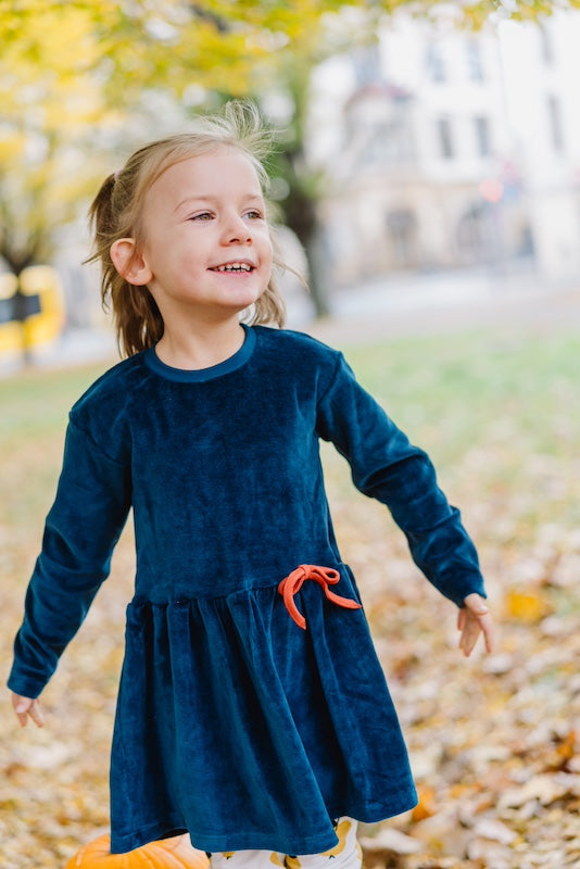 Samtkleid für Mädchen in Dunkelblau aus 100% Biobaumwolle von internaht - Fröhlich lachendes Mädchen im Samtkleid in der Natur