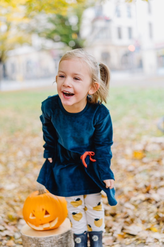 Samtkleid für Mädchen in Dunkelblau aus 100% Biobaumwolle von internaht - Fröhlich lachendes Mädchen im Samtkleid mit Halloween-Kürbis