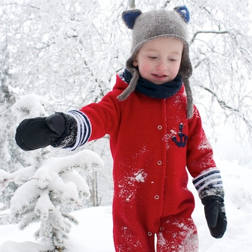 Walkoverall Baby aus Wollwalk in Rot aus 100% Schurwolle von internaht - Praktisch und warm im Herbst & Winter - Kind trägt roten Wollwalk Overall dazu Mütze und Handschuhe und läuft durch eine winterliche, dick beschneite Winterlandschaft